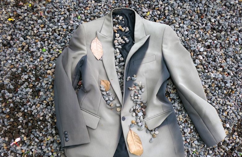 Ein graues Jackett liegt auf Kieselboden. Einige Steinchen und Blätter sind darauf verteilt. Foto: Natalie Baidak