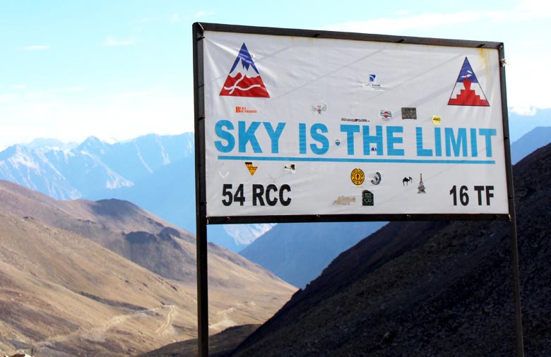 Ein Schild mit der Aufschrift „SKY IS THE LIMIT“ steht an dem Pass. Im Hintergrund sind Gebirge und der strahlend blaue Himmel mit vereinzelten Wölkchen zu sehen. Foto: Jutta Hollands