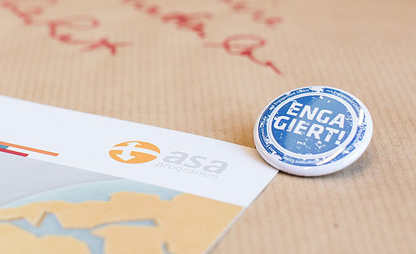 A badge with the word commit yourself and a brochure of the ASA Programme lie on moderation paper.