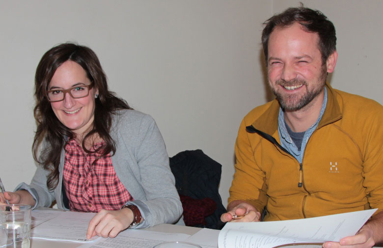 Zwei Personen sitzen an einem Tisch, blättern Bewerbungen durch und lächeln in die Kamera. Foto: Miriam Eckert.