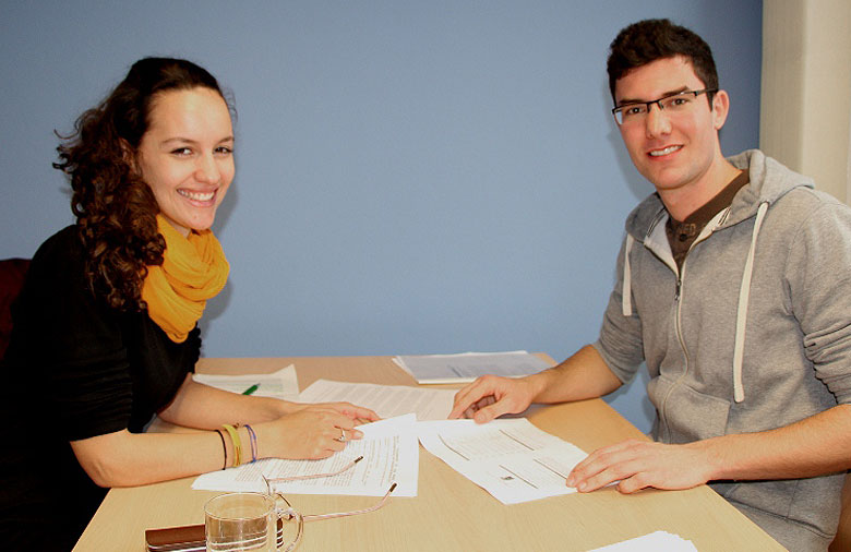 Zwei Personen sitzen an einem Tisch, lesen Bewerbungen und lächeln in die Kamera. Foto: Miriam Eckert.