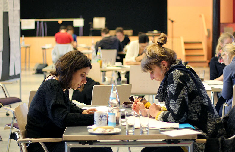Zwei Personen sitzen im Vordergrund an einem Tisch. Sie lesen konzentriert. Im Hintergrund sitzen weitere Personen an Tischen und lesen. Foto: Mira Schönegge
