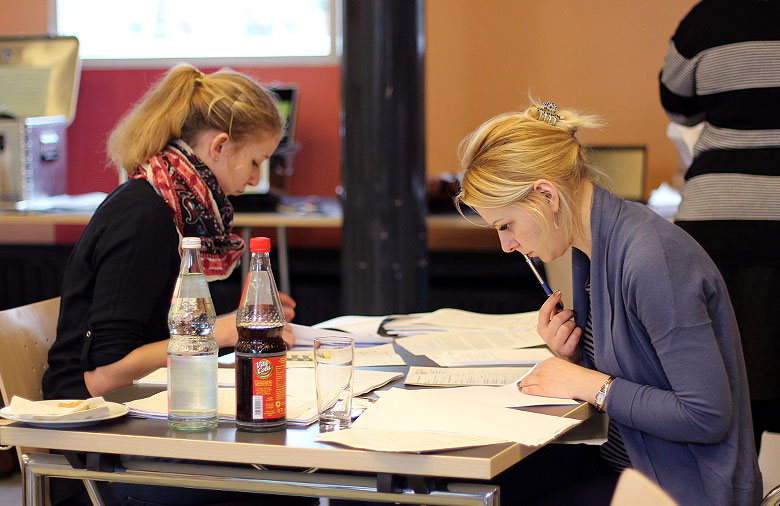 Zwei Personen lesen an einem Tisch sitzend die Bewerbungen. Foto: Mira Schönegge