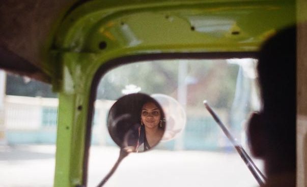 In der Innenansicht eines Autos sieht man das Gesicht einer jungen Frau im Rückspiegel.