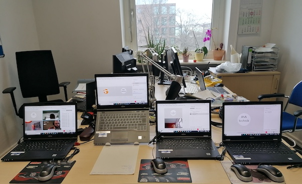 Vier Laptops mit Mousepads sind im Vordergrund abgegbildet. Im Hintergrund befinden sich zwei Büro-Schreibtische.