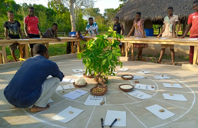 Junge Menschen lernen etwas zu nachhaltiger Landwirtschaft. Der Lehrer sitzt im Kreis und erklärt etwas zu nachhaltigen Anbaumethoden.