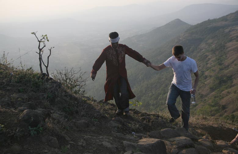 Zwei Männer steigen einen Berg auf und halten sich dabei an der Hand. Im Hintergrund ist eine Gebirgskette zu sehen, die im Nebel verschwindet. Foto: Tim Rödinger