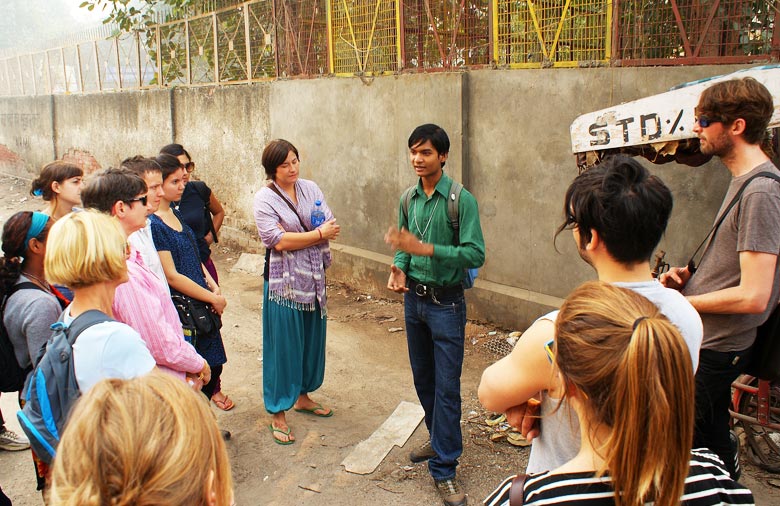 Ein indischer junger Mann als Tour Guide erklärt der umstehenden Touristengruppe etwas. Sie stehen auf einer Straße, hinter ihnen ist eine Mauer. Foto: Jens Marquardt