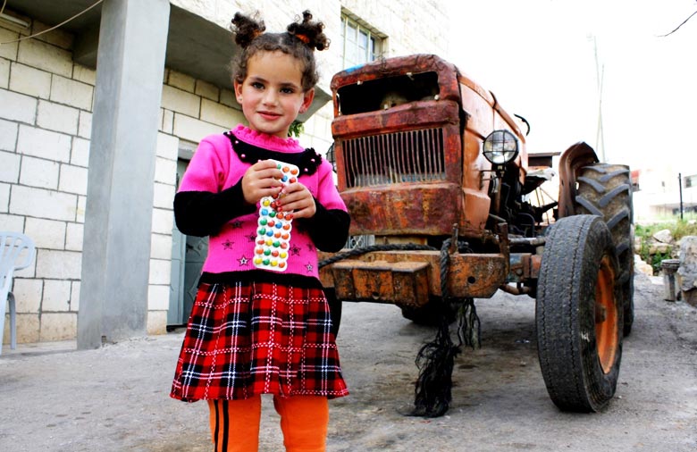 Ein kleines Mädchen mit einer Kaugummipackung  in ihren Händen, steht auf einem Hof. Im Hintergrund ist ein Trecker zu sehen. Foto: Antje Grebing.