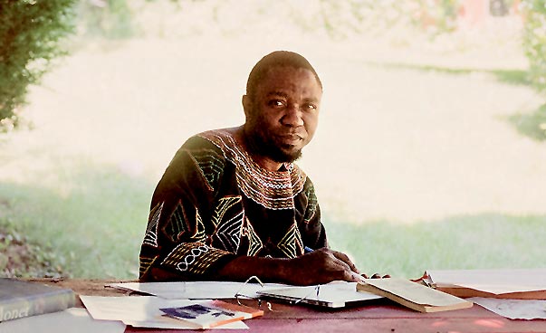 Das Foto zeigt Alain Patrice Nganang. Er sitzt im Schatten eines Baumes an einem Tisch. Foto: Alain Patrice Nganang