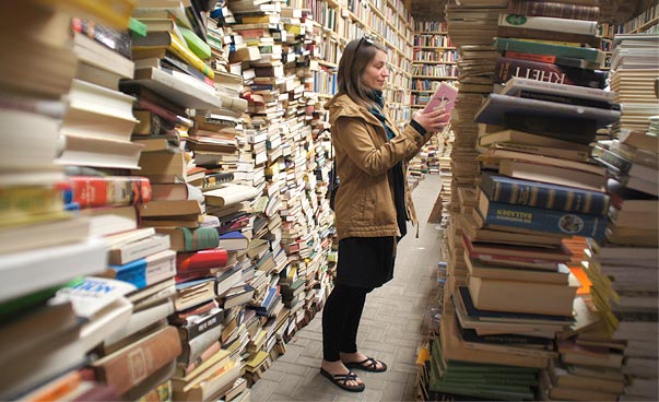 Eine Person steht inmitten von Bücherstapeln und liest. Foto: Bernadette Lier