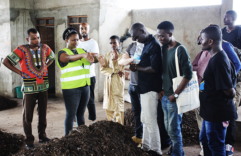 A woman explains a procedure to a group of people in front of brownish piles