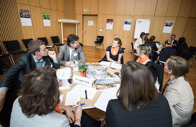 Ludger Eltrop sitzt mit Teilnehmenden an einem Tisch im Seminarraum und diskutiert. Foto: Christian Klant.