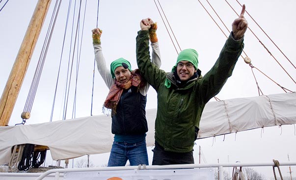 Two people raise their hands together. They are on a ship.